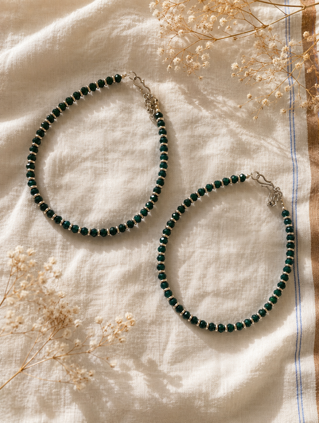 Green beaded anklet on a textured fabric background with dried flowers
