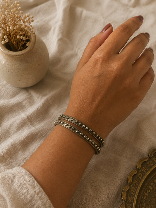 Hand wearing a bracelet on a light fabric background with a small vase and decorative item.