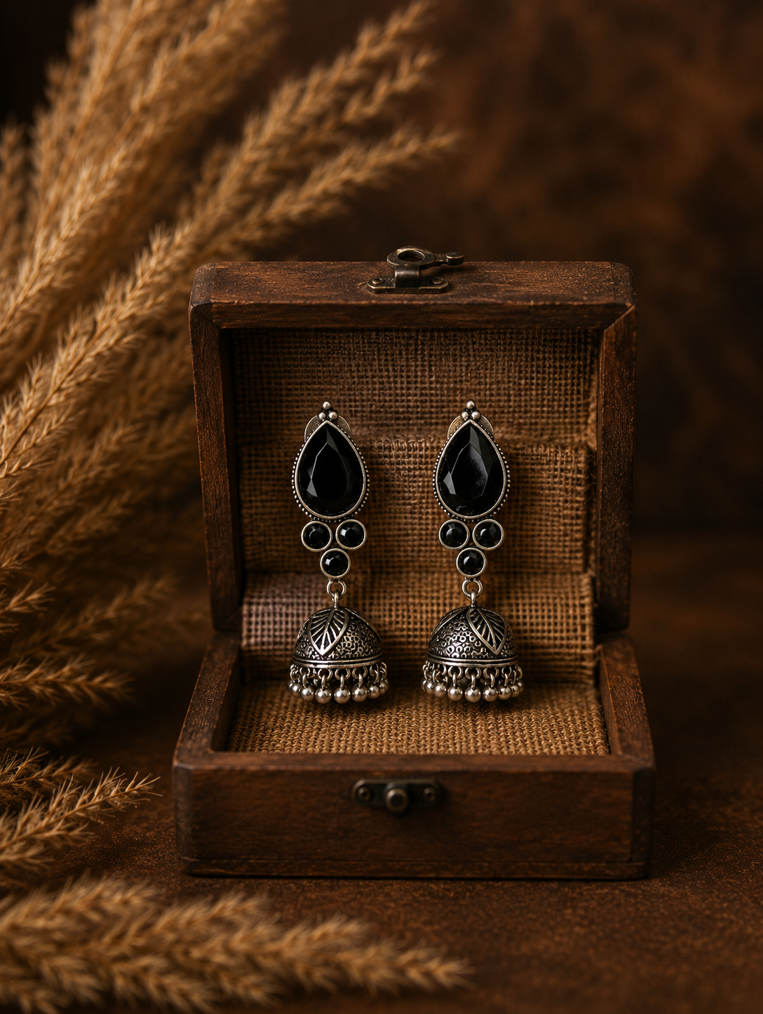 Pair of black teardrop earrings with gold accents in a wooden box on a textured brown background