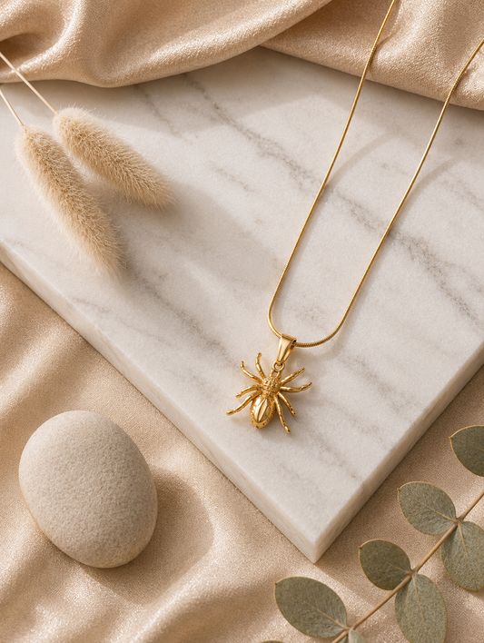 A collection of three product photographs showcasing a detailed gold-tone spider pendant necklace on a fine snake chain, styled in both a warm flat lay on a white marble slab and displayed on a beige velvet jewelry bust.