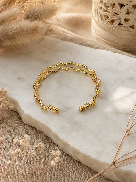 Gold bracelet on a marble surface with natural elements