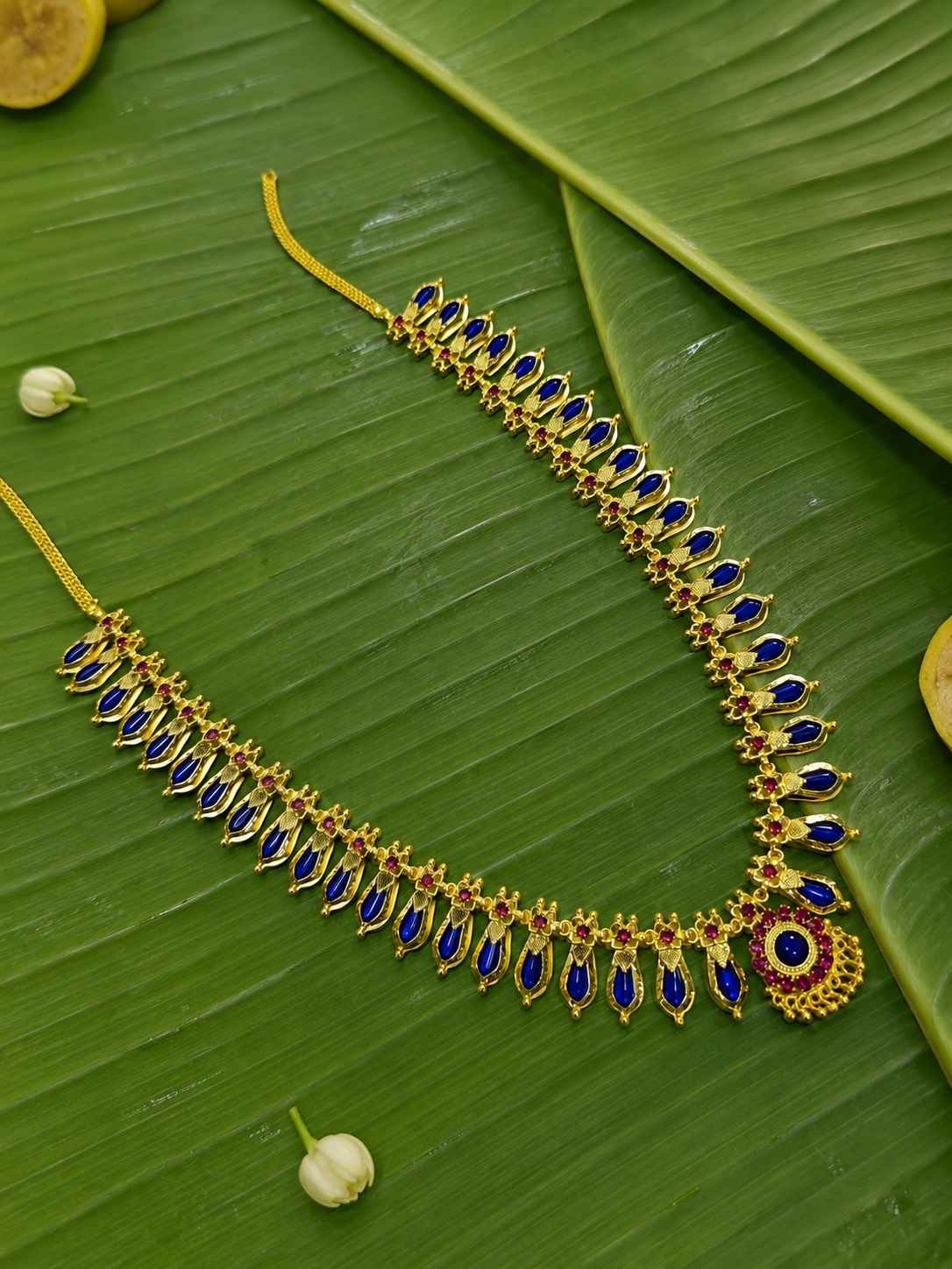 Traditional blue stone Kerala Nagapadam necklace with a circular ruby-bordered pendant, showcased as a flat lay on a natural banana leaf.