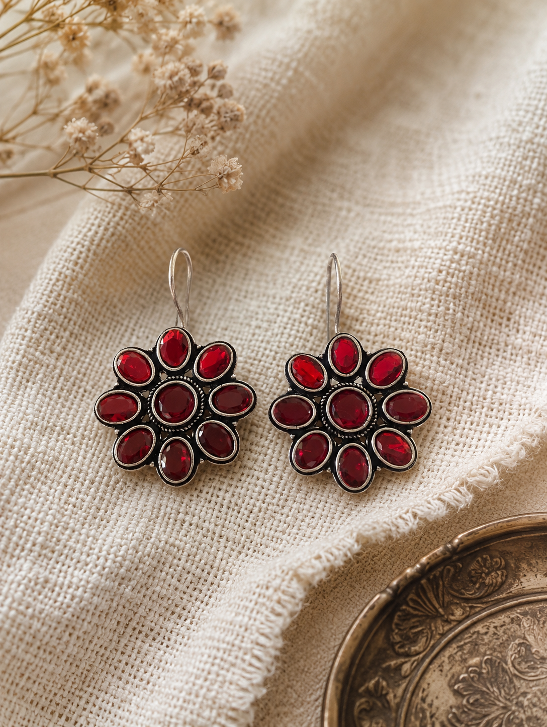 Pair of red floral earrings on a textured beige fabric background