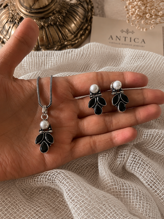 Hand holding a necklace and earrings with 'ANTICA' branding in the background
