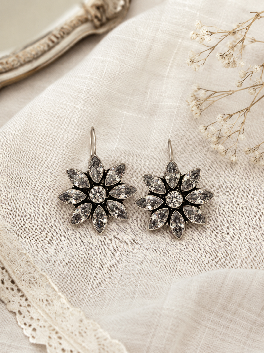 Pair of silver floral earrings on a textured fabric background