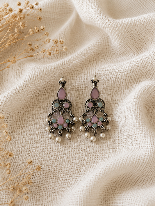 Pair of ornate earrings with gemstones on a textured beige fabric background