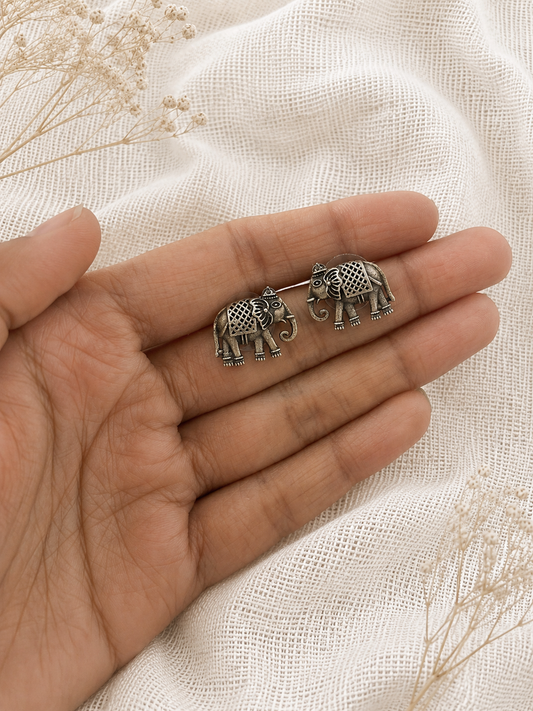 Two silver elephant earrings held between fingers on a light fabric background
