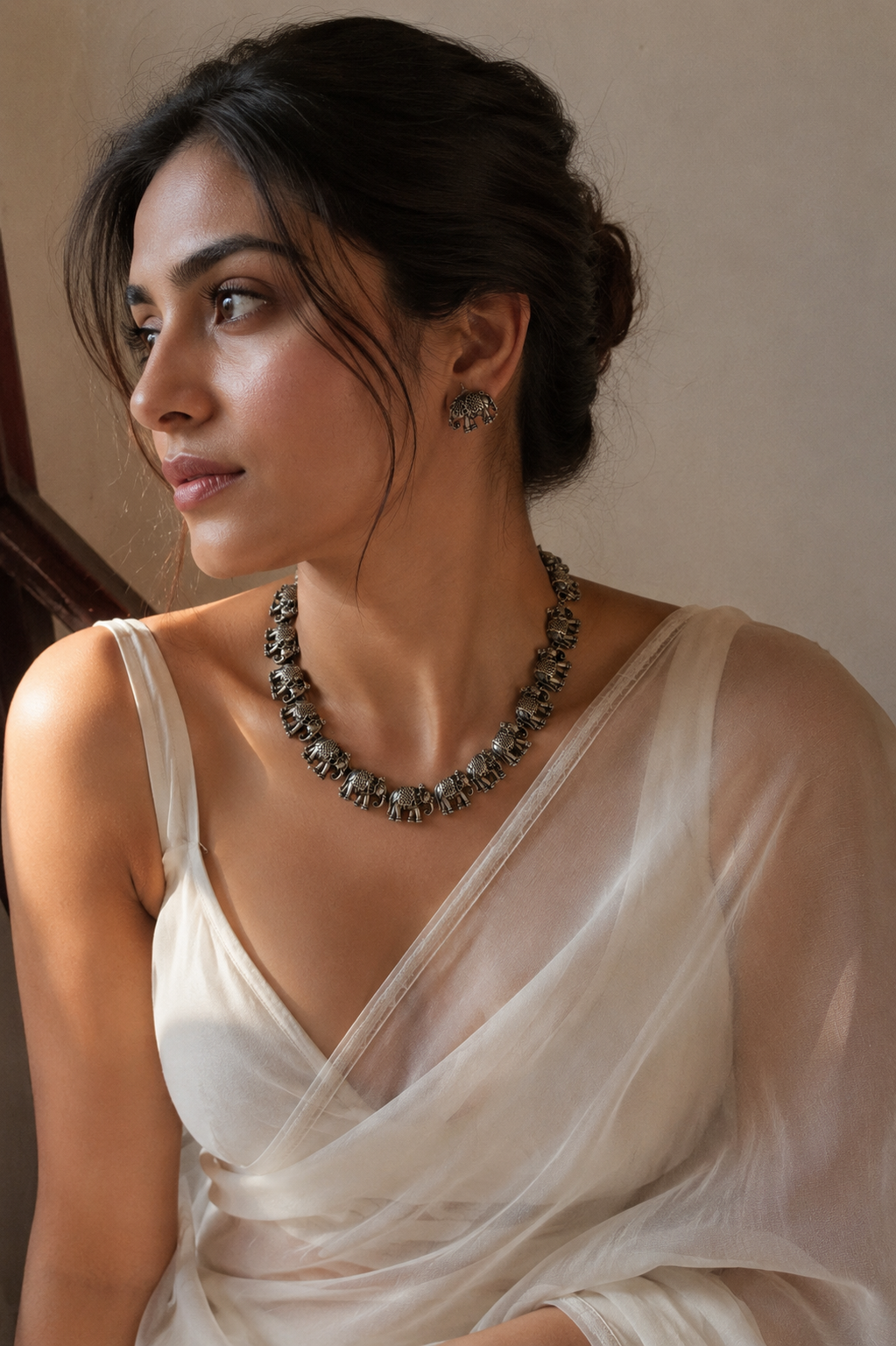 Woman wearing a white saree with a necklace and earrings against a neutral background