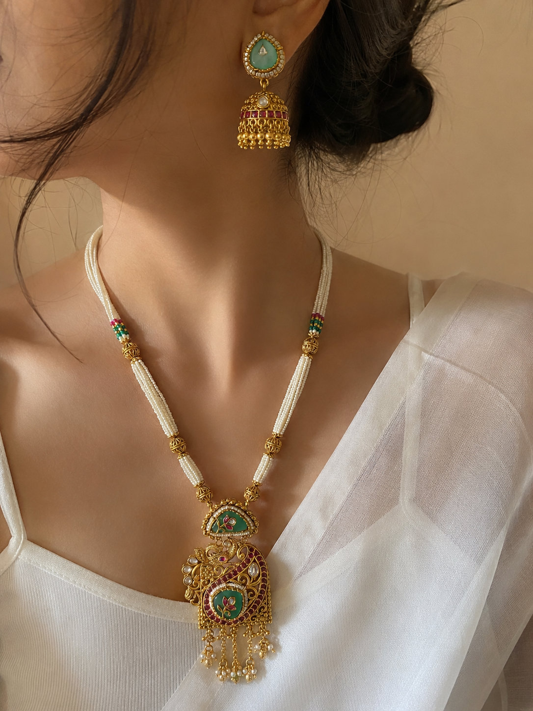 Close-up of a person wearing an ornate necklace and earrings with a neutral background