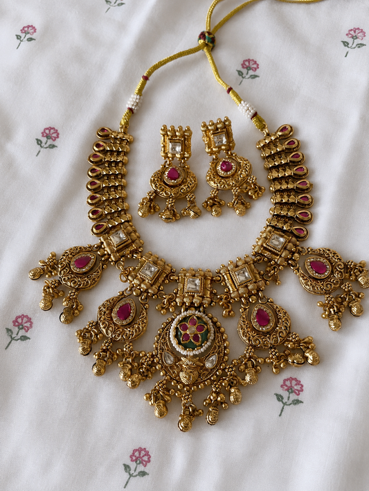 Gold necklace and earrings set on a floral-patterned fabric background