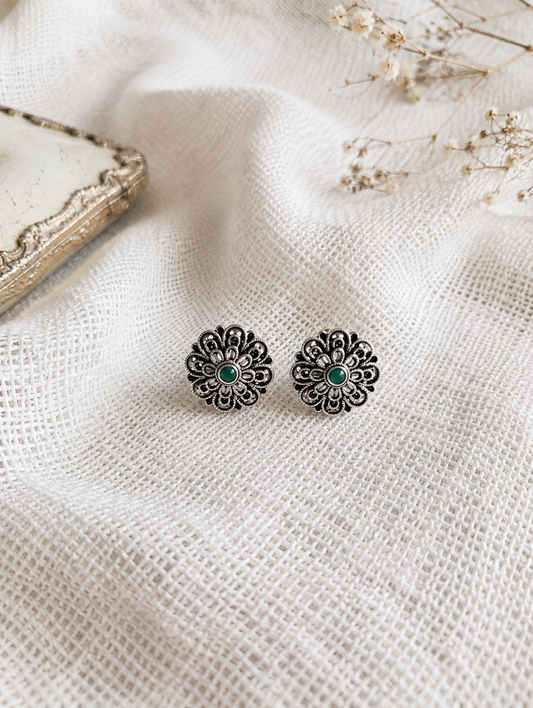 Floral earrings with green centers on a textured white fabric background