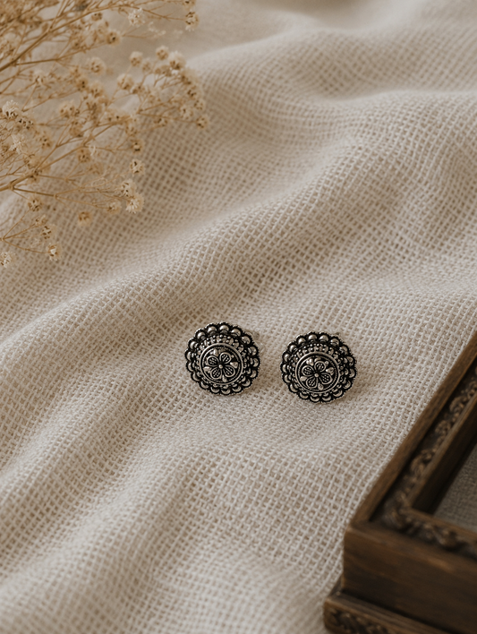Pair of silver floral earrings on beige fabric with dried flowers.