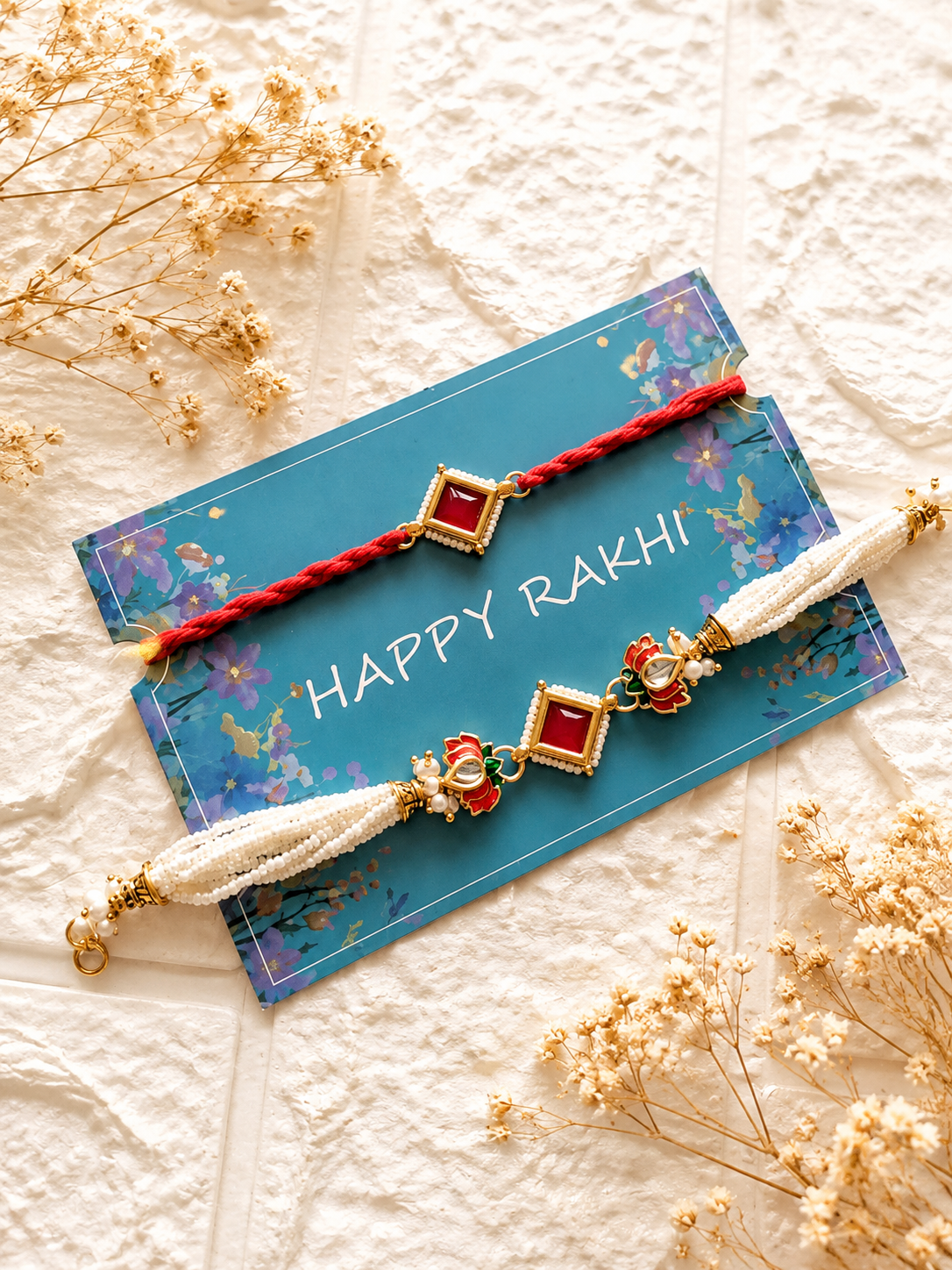 Handcrafted Bhaiya Bhabhi Rakhi set featuring a multi-strand pearl Lumba bracelet with lotus charms and a matching red thread Rakhi on a blue card.