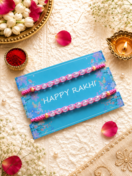 Set of two pink woven Rakhi bracelets studded with faceted clear crystal beads and gold accents displayed on a blue Happy Rakhi card.