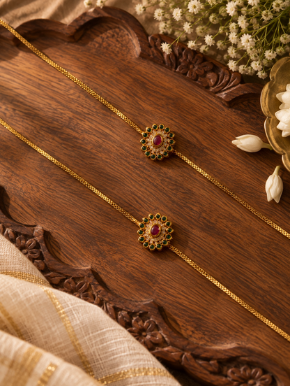 Pair of traditional gold-plated floral Kundan anklets with green and red gemstone floral pendants displayed on a carved wooden tray.