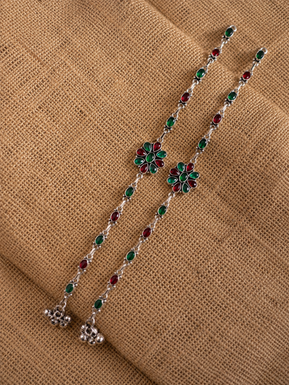 Silver chain with green and red floral pendants on a brown fabric background
