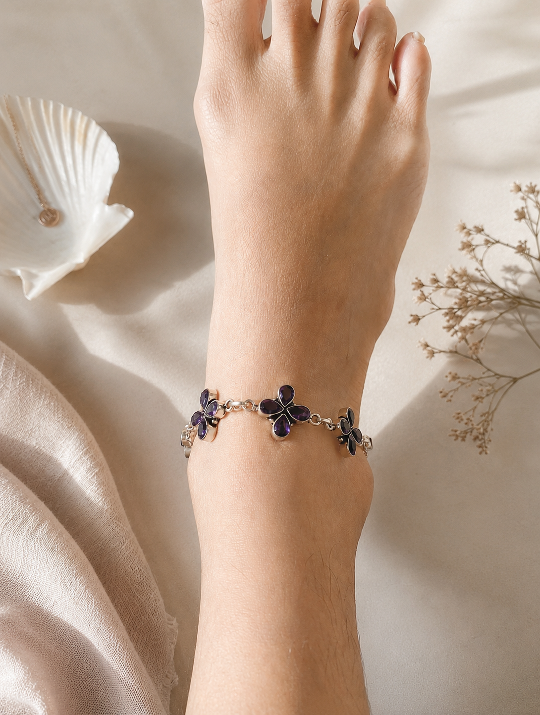 Leg wearing a anklet with purple flower charms on a soft beige background
