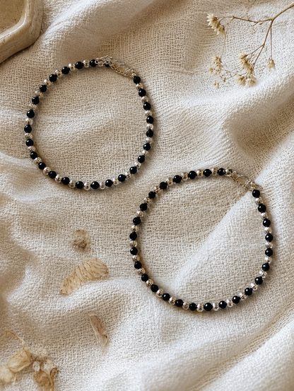 Two beaded Anklets on a textured beige fabric background with dried flowers.