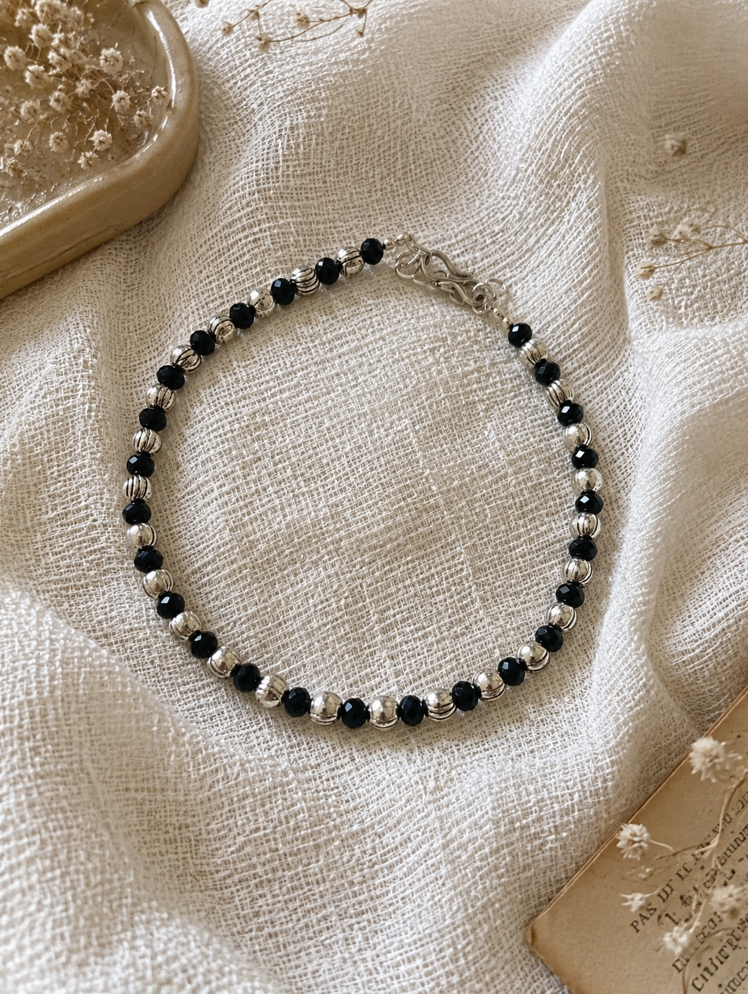 Beaded anklet with black and clear beads on a textured beige surface
