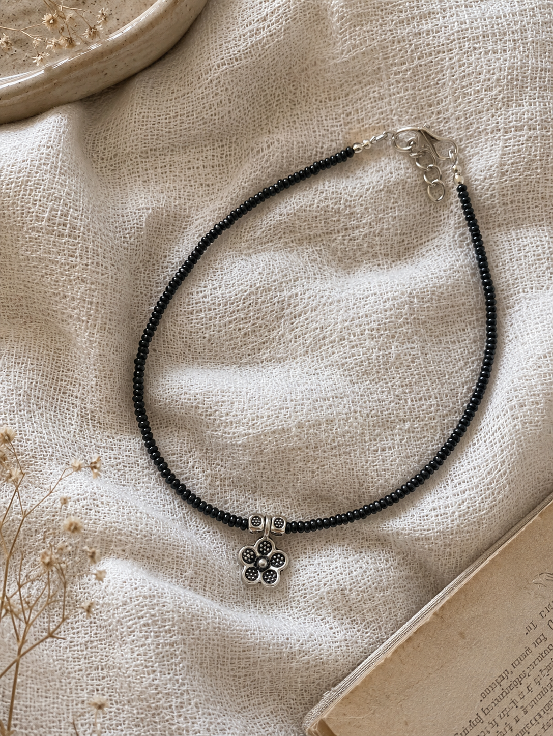 Anklet with a flower charm on a textured beige surface