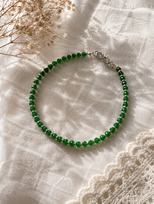 Green beaded anklet on a textured white surface with dried flowers.