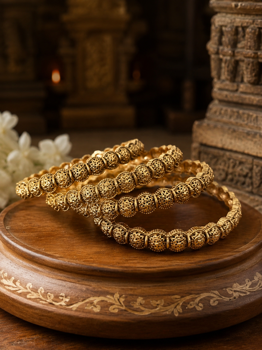 Two gold bracelets on a wooden stand with a decorative background