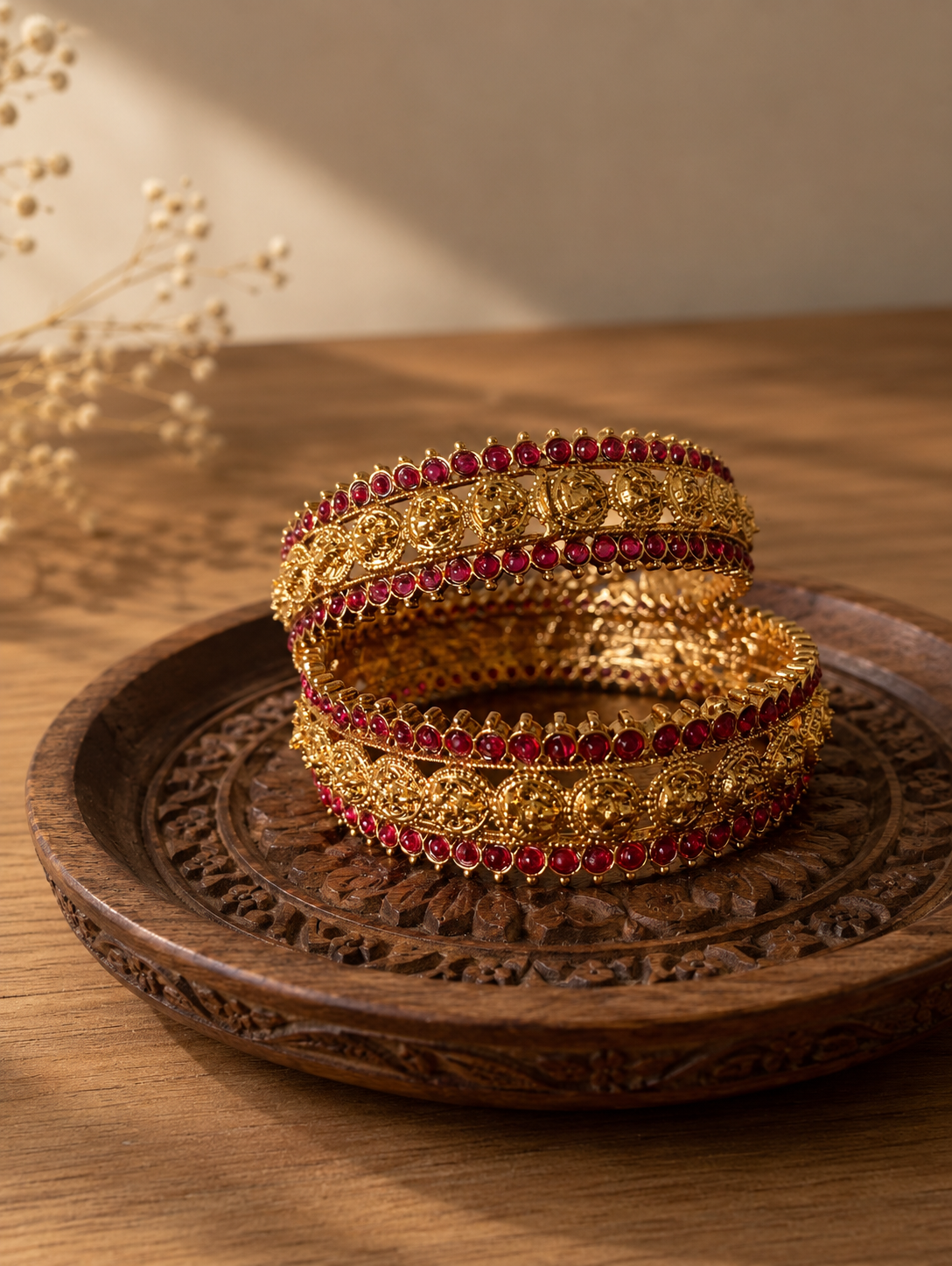 Gold bangles with red stones on a wooden tray