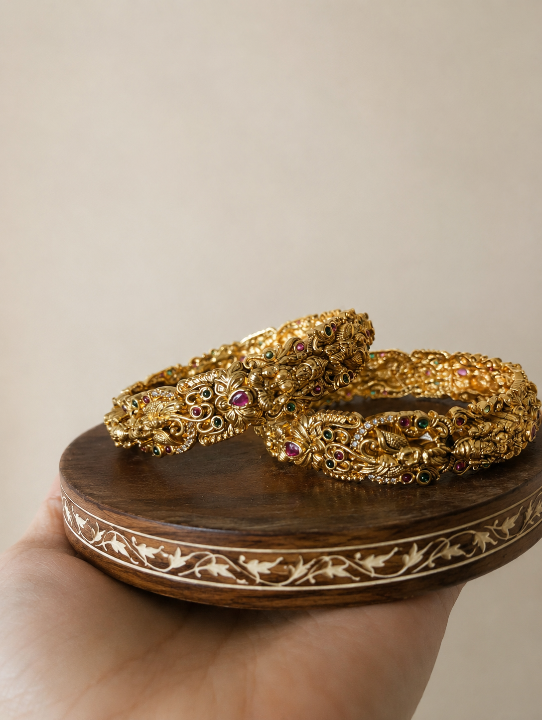 Two gold bangles on a wooden stand with a beige background