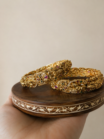 Two gold bangles on a wooden stand with a beige background