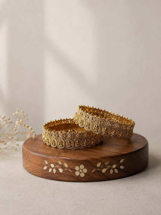 Two gold bracelets on a wooden stand with a beige background