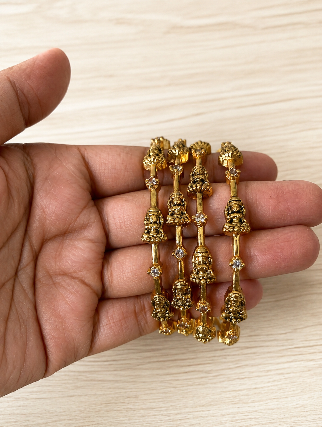 Gold jewelry set held in a hand on a light wooden surface