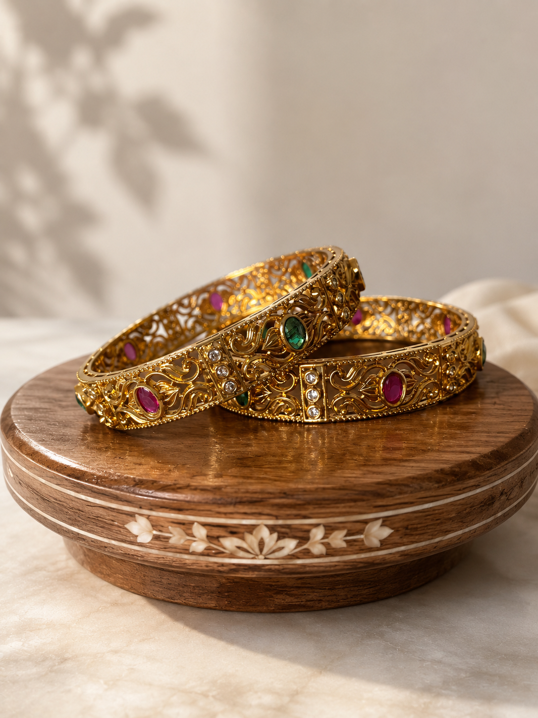 Two gold bangles with gemstones on a wooden dish