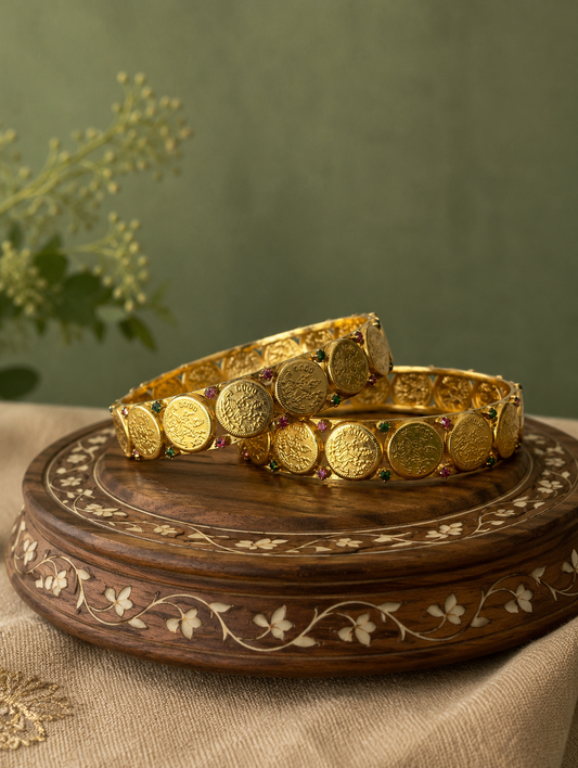 Two gold bangles on a wooden stand with a green background