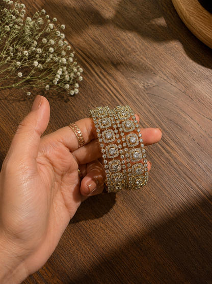 Hand holding a decorative bracelet on a wooden surface with dried flowers.
