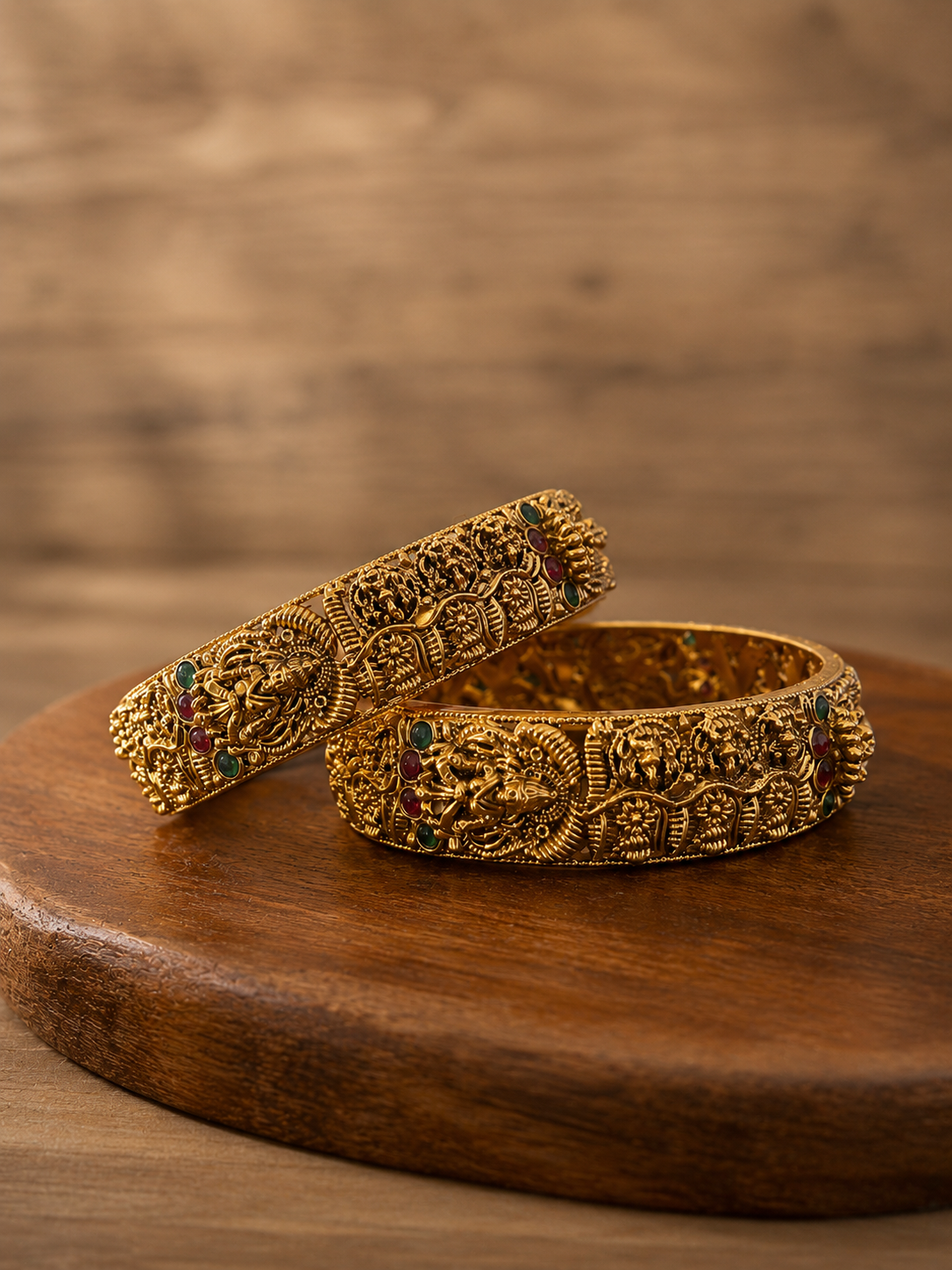 Two ornate gold bangles on a wooden surface with a blurred brown background