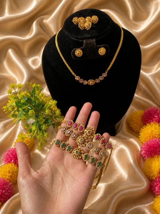 Gold jewelry set including necklace, earrings, and bangles on a black velvet stand with a hand holding the jewelry against a satin background.