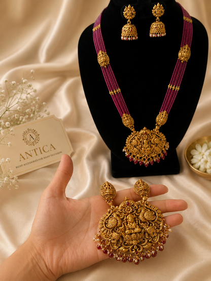 Long multi-strand pink beaded temple jewelry necklace with a large intricate golden pendant and matching jhumka earrings displayed on a black bust.