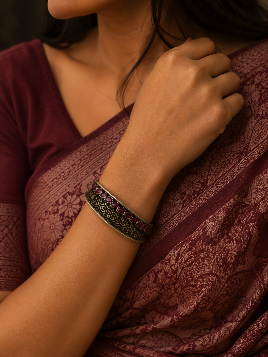 Close-up of a person wearing a maroon saree with a bracelet featuring red stones.