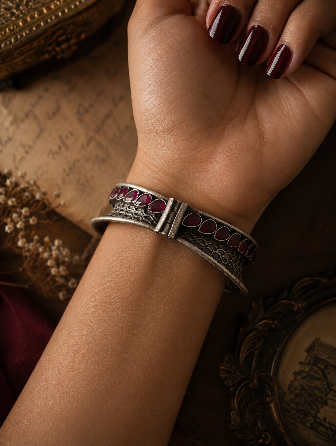 Silver bracelet with red stones on a wrist against a textured background