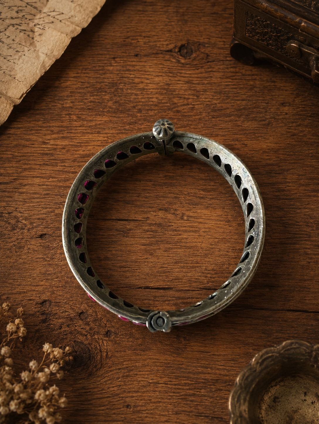 Silver bracelet on a wooden surface with dried flowers and an old book.