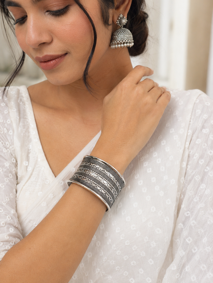 Woman wearing silver jewelry including bangles and earrings, dressed in a white outfit.