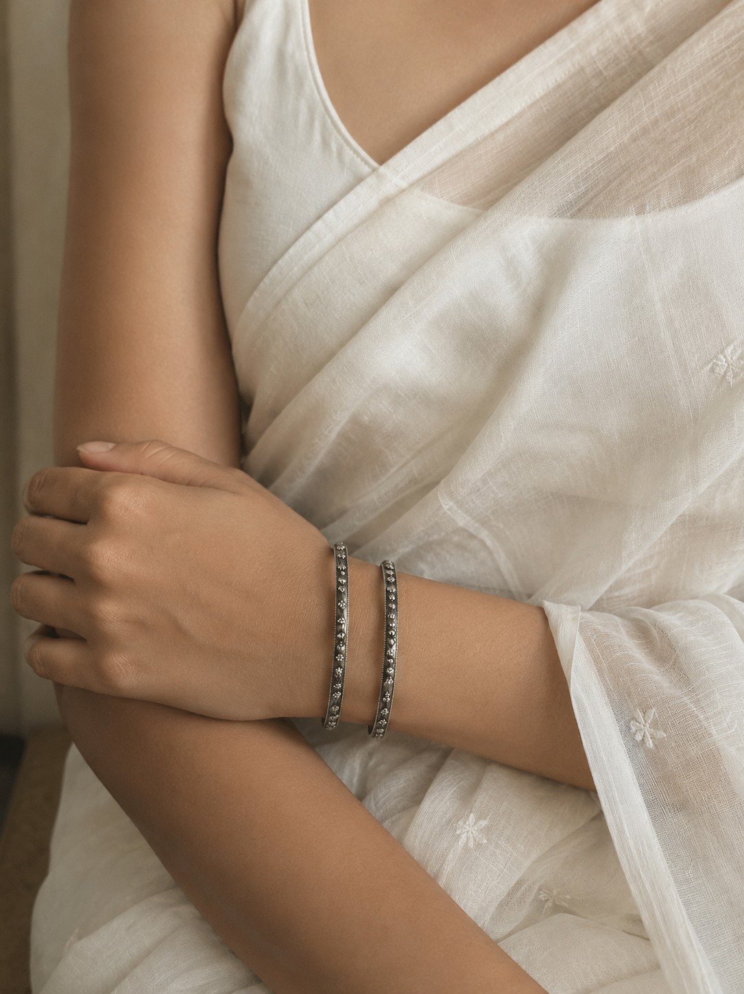 Person wearing a white saree with a close-up of their arm and bracelet.