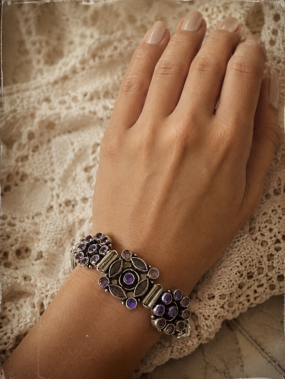 Hand wearing a decorative bracelet with purple stones on a textured fabric background