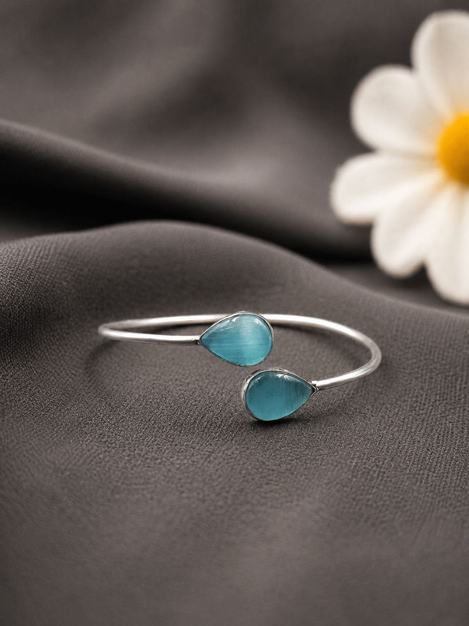 Silver bracelet with blue teardrop charms on a dark fabric background with a white flower.