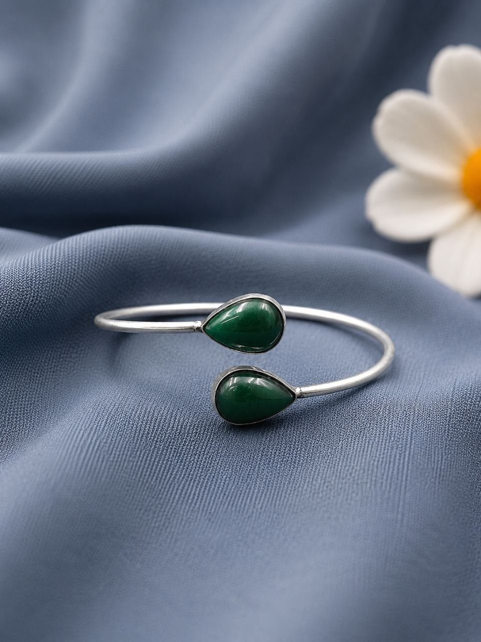 Silver bracelet with green stones on a blue fabric background