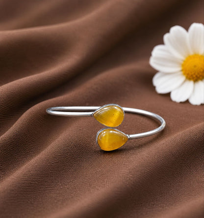 Silver bracelet with yellow teardrop stones on brown fabric with a white flower.