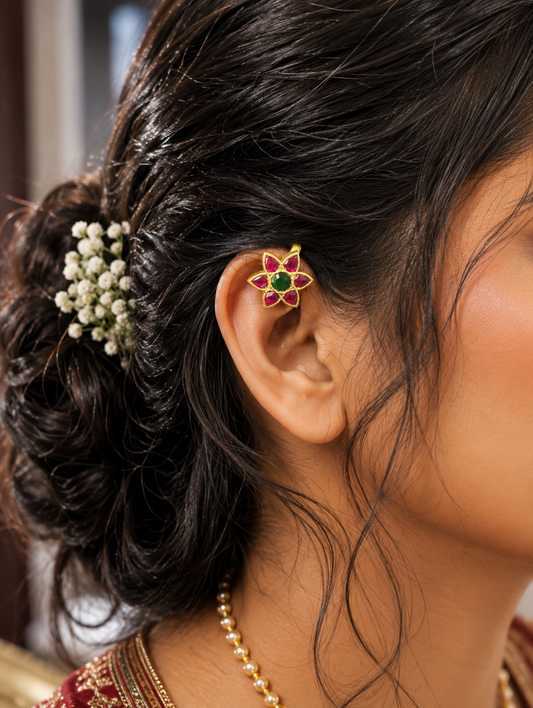 Close-up of a model wearing a traditional gold floral Bugudi clip-on cuff on her upper ear helix, styled with an elegant updo hairstyle and baby's breath flowers.
