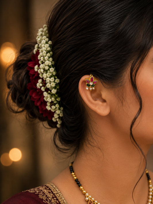 A woman wearing a traditional gold floral kemp stud ear cuff on her upper ear cartilage, with her hair styled in an elegant bun decorated with fresh white flowers.