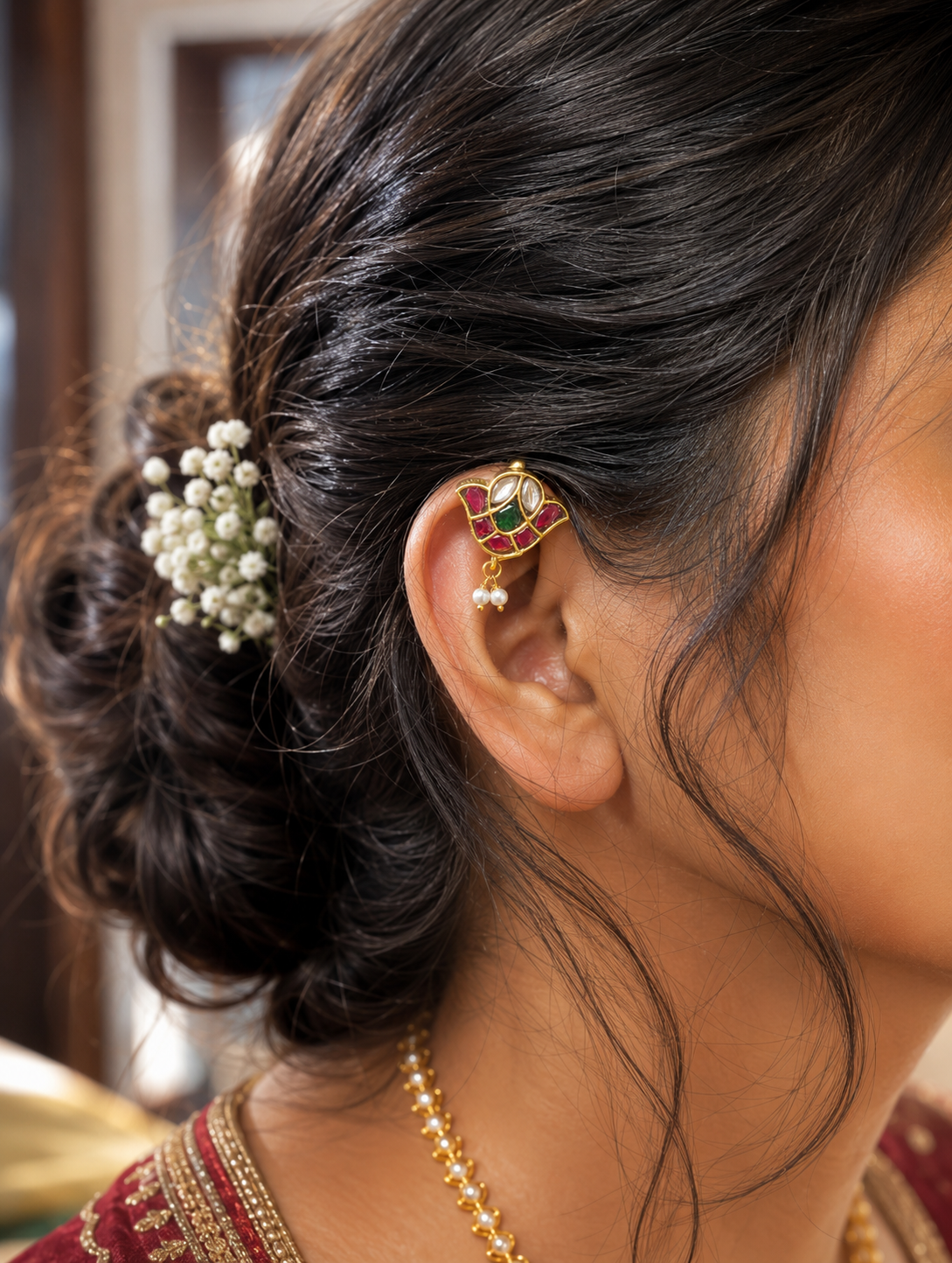 Side profile of a woman wearing a traditional gold floral Jadau Kundan bugudi ear cuff on her upper ear cartilage, beautifully completing a bridal look with a textured hair updo adorned with white flowers.