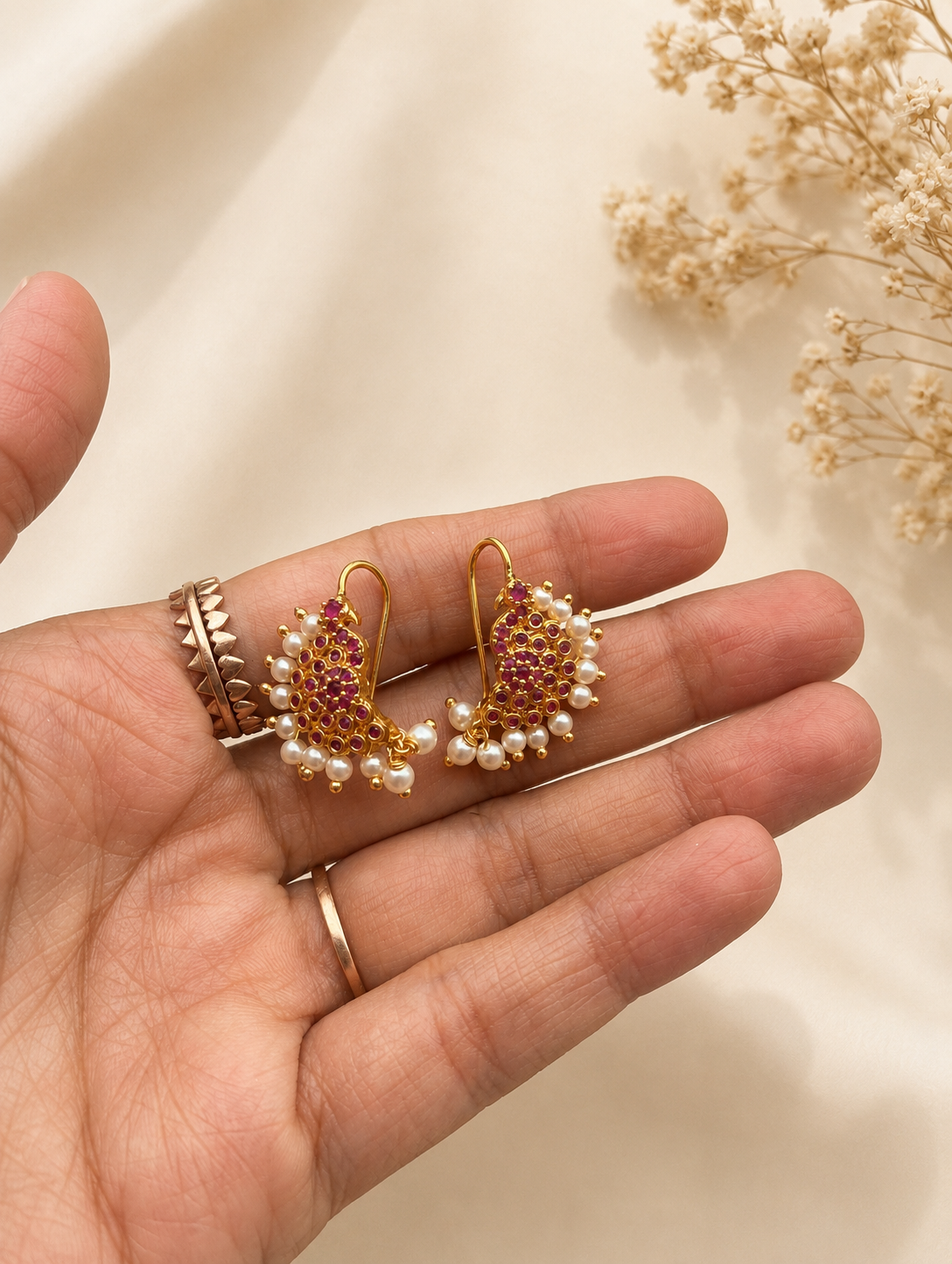 A pair of traditional gold-plated Gili Ole inspired Bugudi ear cuffs featuring a dense setting of tiny ruby red stones and a delicate border of white pearls, displayed on a hand.